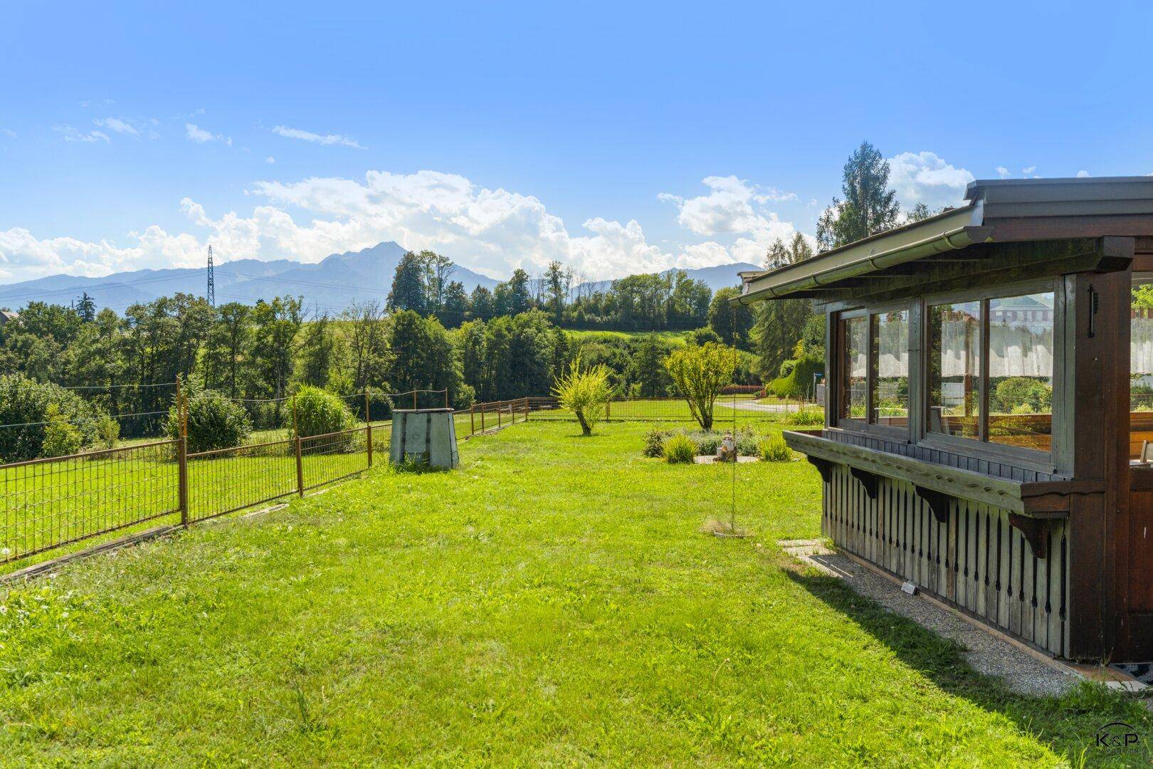 Großer grüner Garten mit einer kleinen Holzkonstruktion und weitem Blick auf die umliegende Berglandschaft.