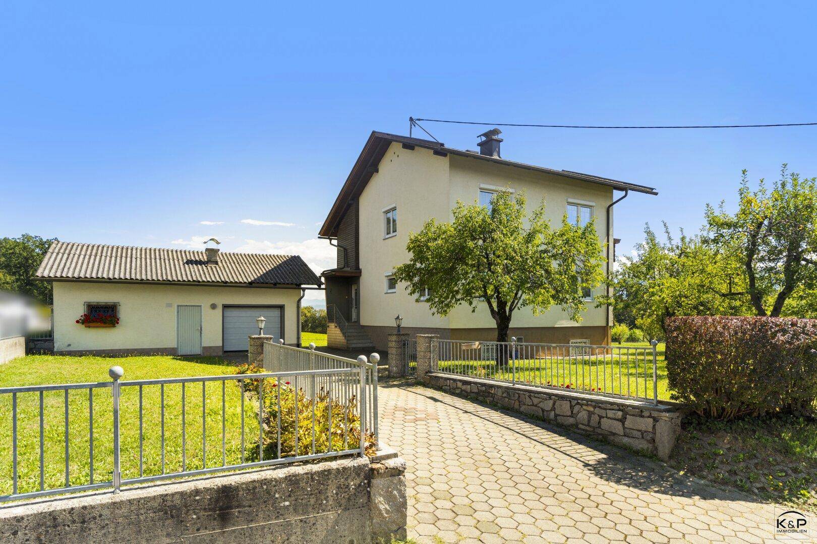 Vorderansicht des Hauses mit Garage und gepflasterter Auffahrt, umgeben von einem grünen Garten.