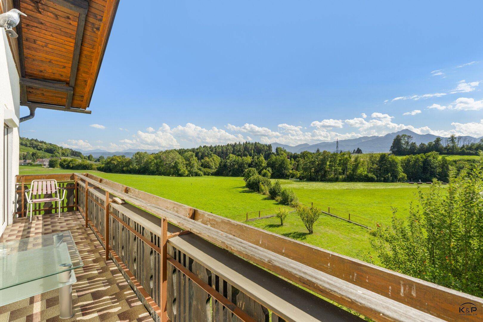 Geräumiger Balkon mit Holzboden und einem weiten, unverbauten Blick auf grüne Felder und Berge.
