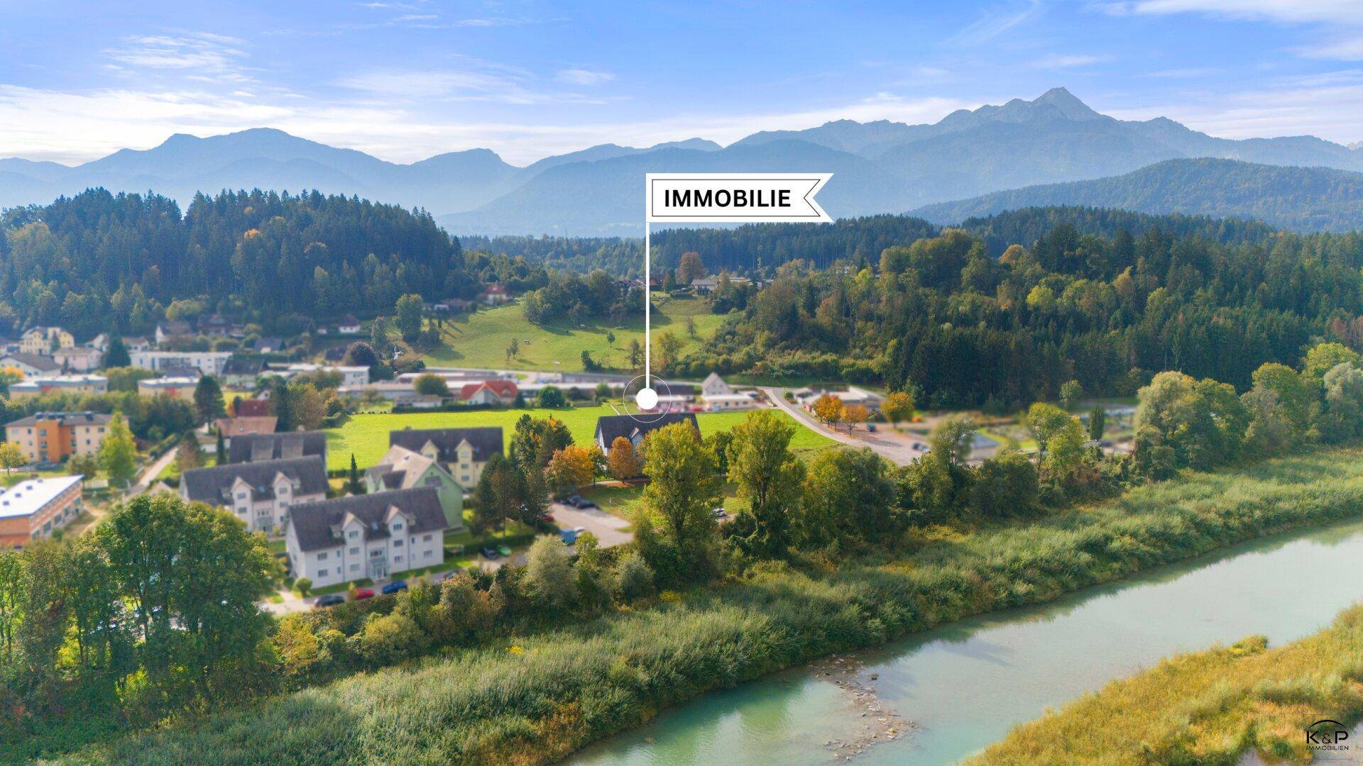 Weitläufige Luftaufnahme der Immobilie in einer grünen Landschaft mit beeindruckendem Bergpanorama.