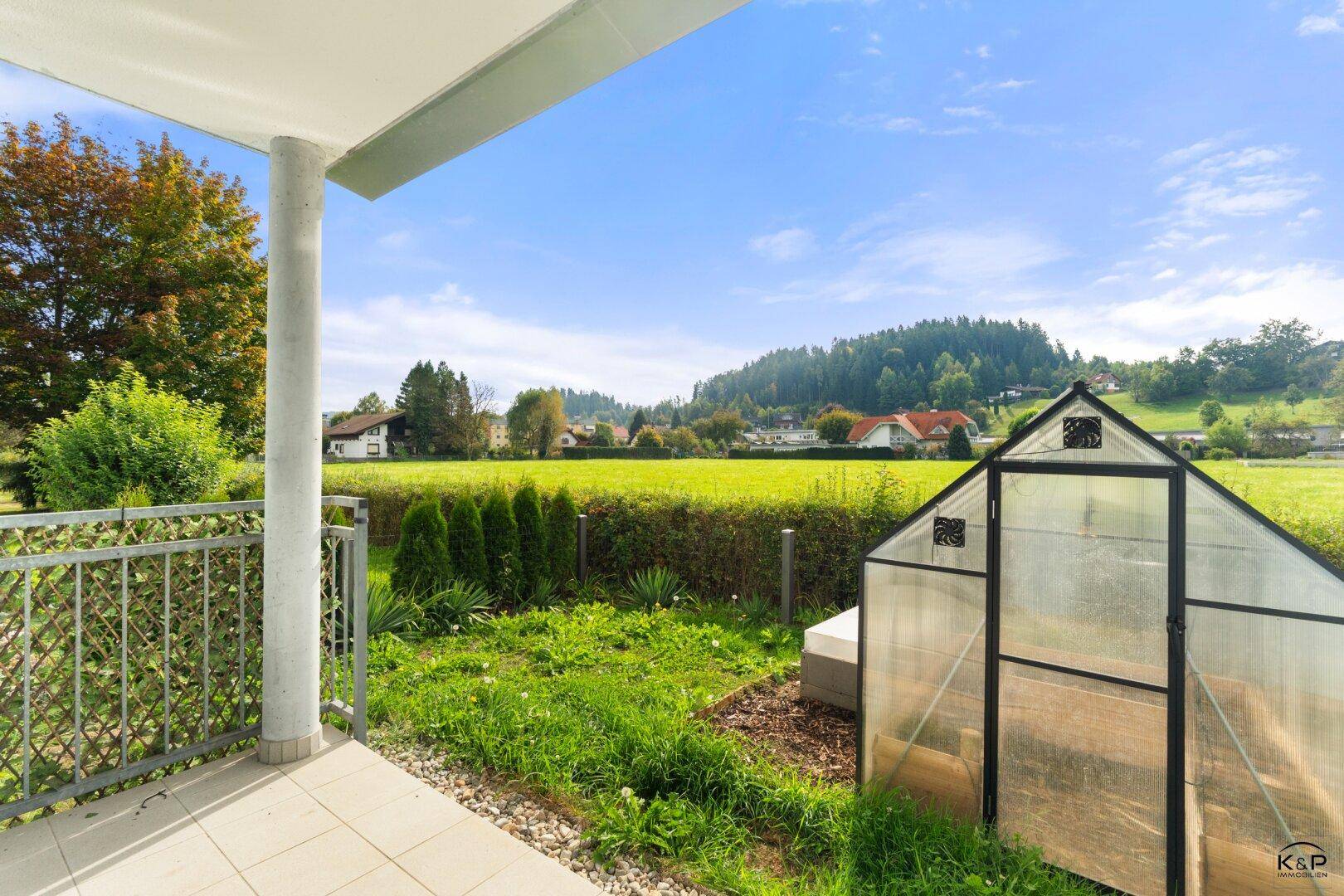 Geräumige Terrasse mit weitem Blick über den Garten, das Gewächshaus und die umliegende Natur.