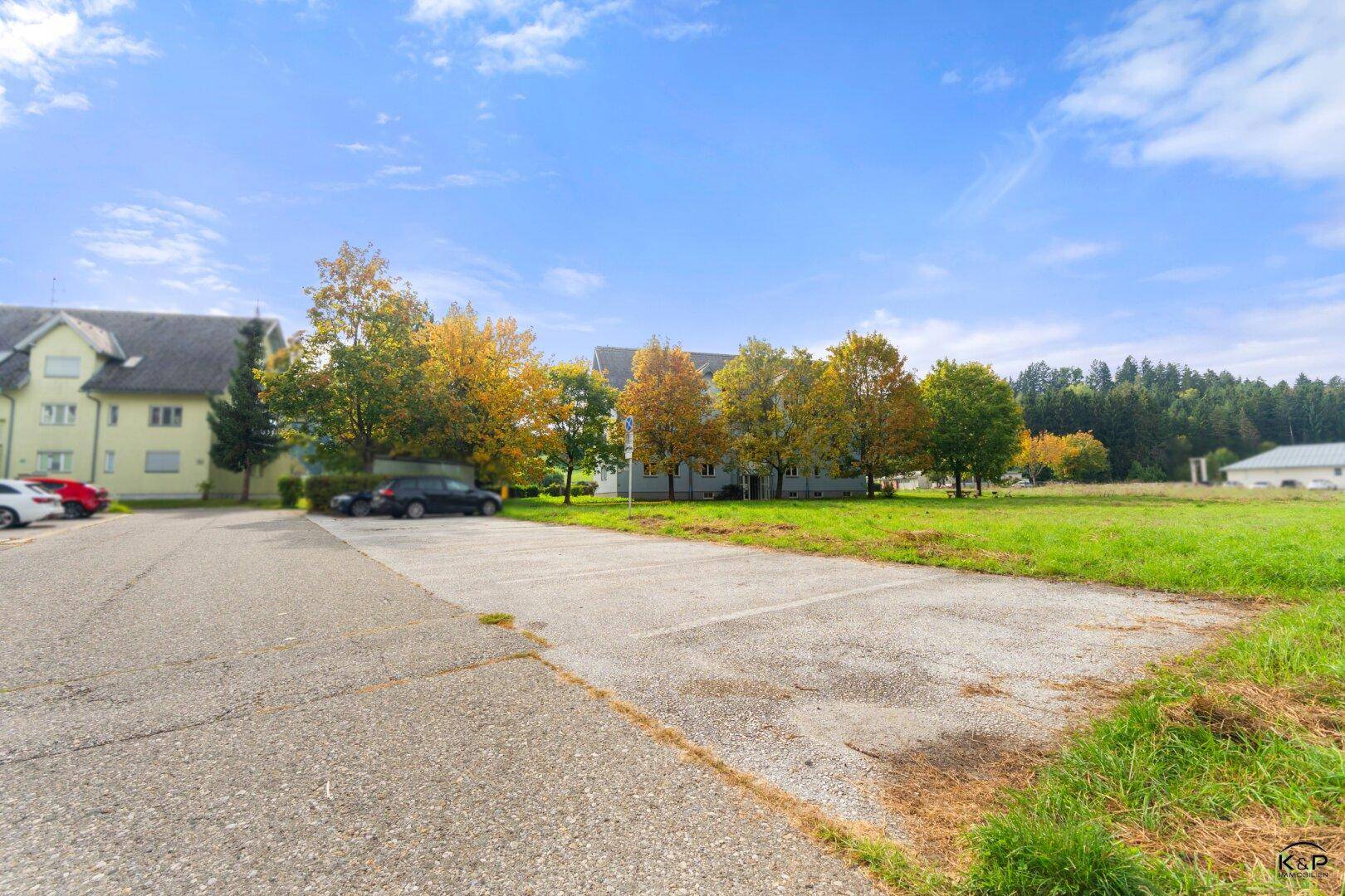 Außenparkplatz neben dem Gebäude, umgeben von weiten Grünflächen und Bäumen.