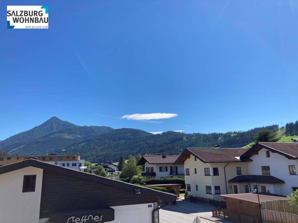 Weitläufiger Blick auf die umliegende Berglandschaft und benachbarte Gebäude unter blauem Himmel.