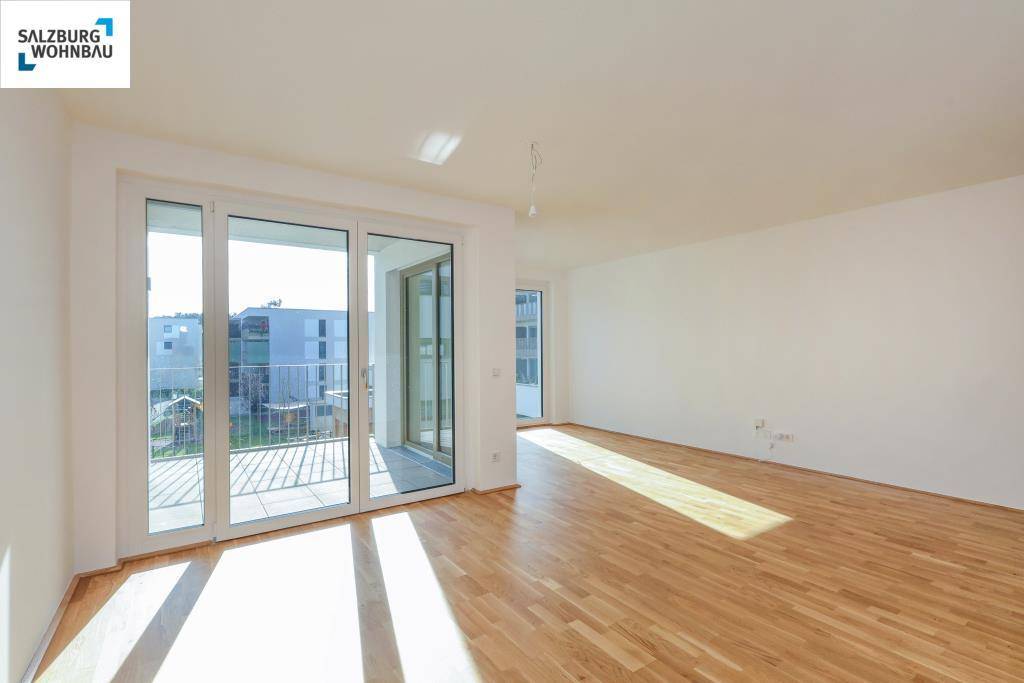 Lichtdurchfluteter Raum mit Holzboden und breiten Schiebetüren, die Zugang zu einem Balkon bieten.