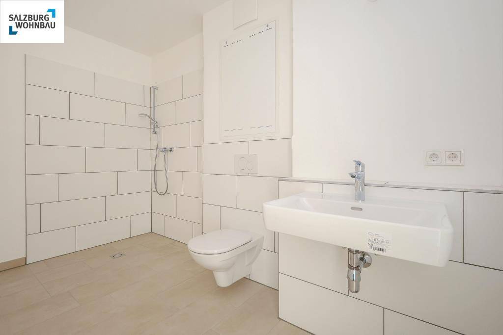 Modernes Badezimmer mit ebenerdiger Dusche, wandhängendem WC und weißem Waschbecken.