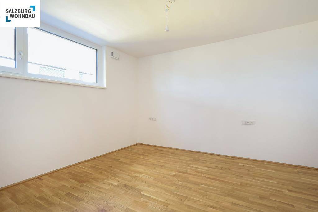 Helles Schlafzimmer mit Holzboden und einem großen Fenster, das viel Tageslicht spendet.