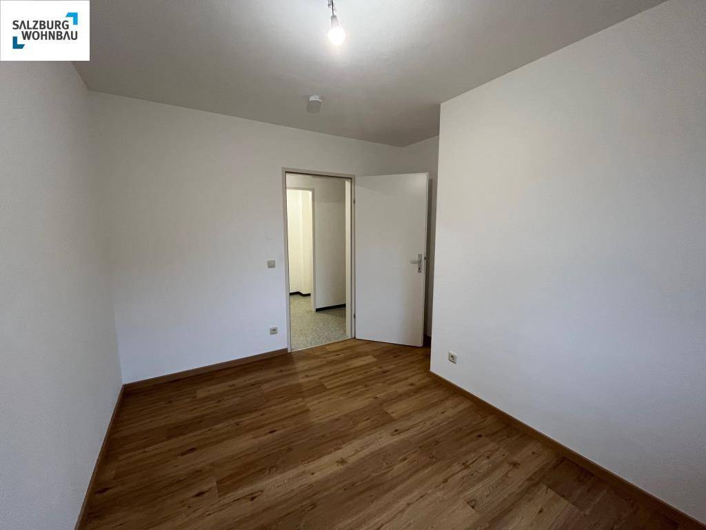 Leeres Schlafzimmer mit Laminatboden und weiß gestrichenen Wänden, bietet viel Gestaltungsfreiheit.