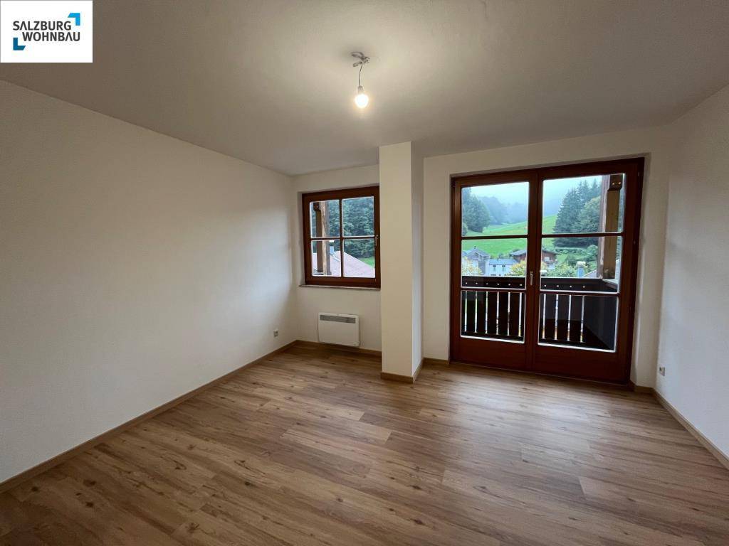 Helles Zimmer mit Laminatboden und Zugang zu einem Balkon, bietet eine schöne Aussicht auf die Natur.