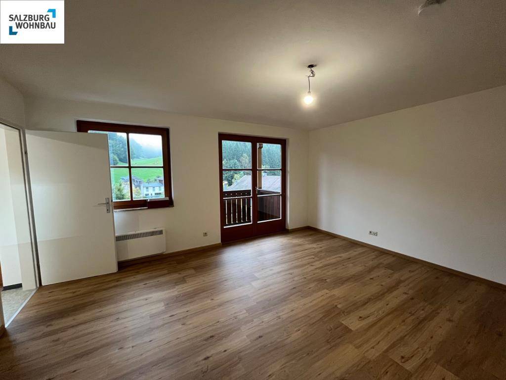 Helles Wohnzimmer mit Laminatboden, Fenster und Balkonzugang, bietet Blick ins Grüne.