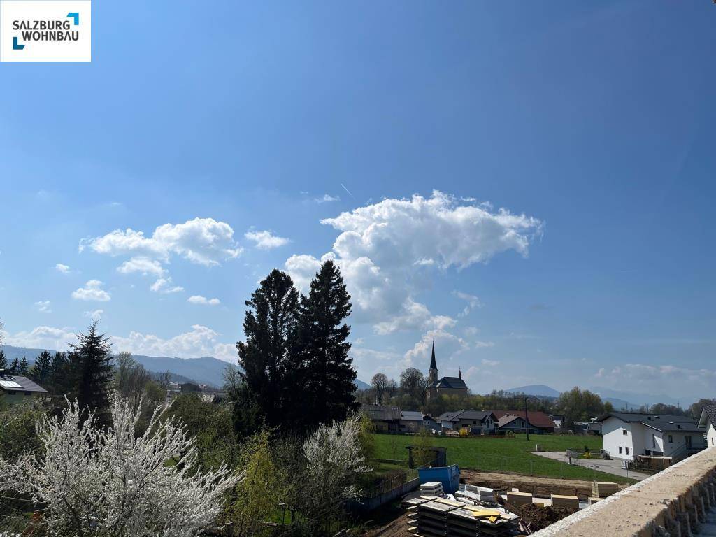 Blick auf eine ländliche Umgebung mit Dorf, Bergen und blühenden Bäumen unter blauem Himmel.