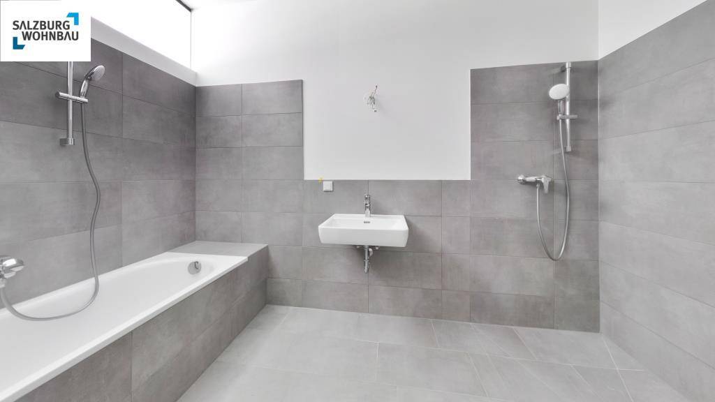 Modernes Badezimmer mit grauen Fliesen, Badewanne und separater Dusche, funktional und hell gestaltet.
