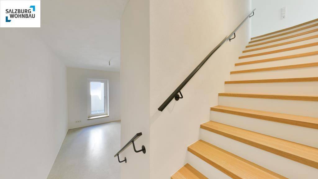 Heller Flur mit Holztreppe und modernem Geländer, der zu weiteren Räumen im Haus führt.