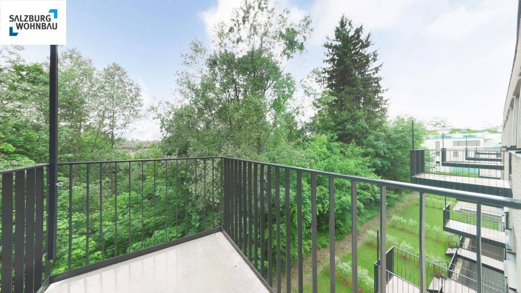 Kleiner Balkon mit schwarzem Geländer und Blick ins Grüne mit hohen Bäumen.