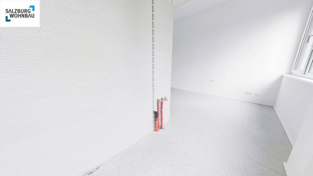 Leerer Raum mit weißen Wänden, Betonboden und sichtbaren Installationen für zukünftige Nutzung.