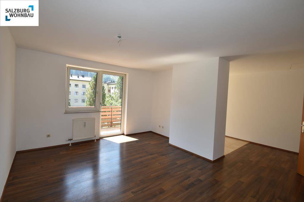 Heller Wohnraum mit dunklem Laminatboden, weißen Wänden und Zugang zu einem Balkon.