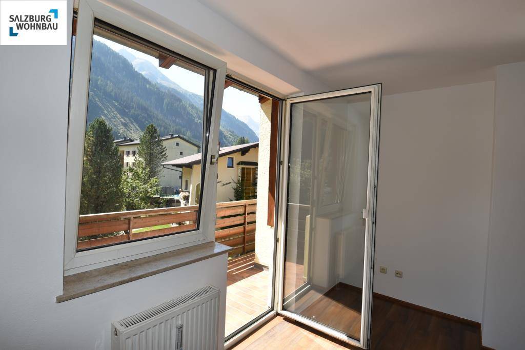 Blick aus dem Wohnzimmer auf einen Holzbalkon und die umliegende Berglandschaft.