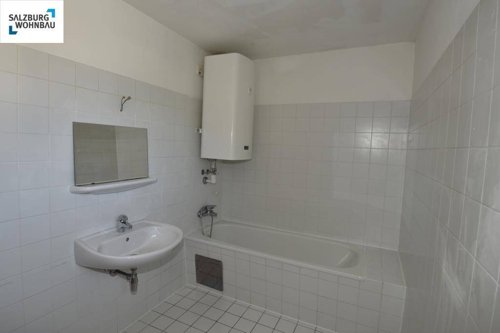 Gefliestes Badezimmer mit Badewanne, Waschbecken und Warmwasserboiler in schlichtem Design.