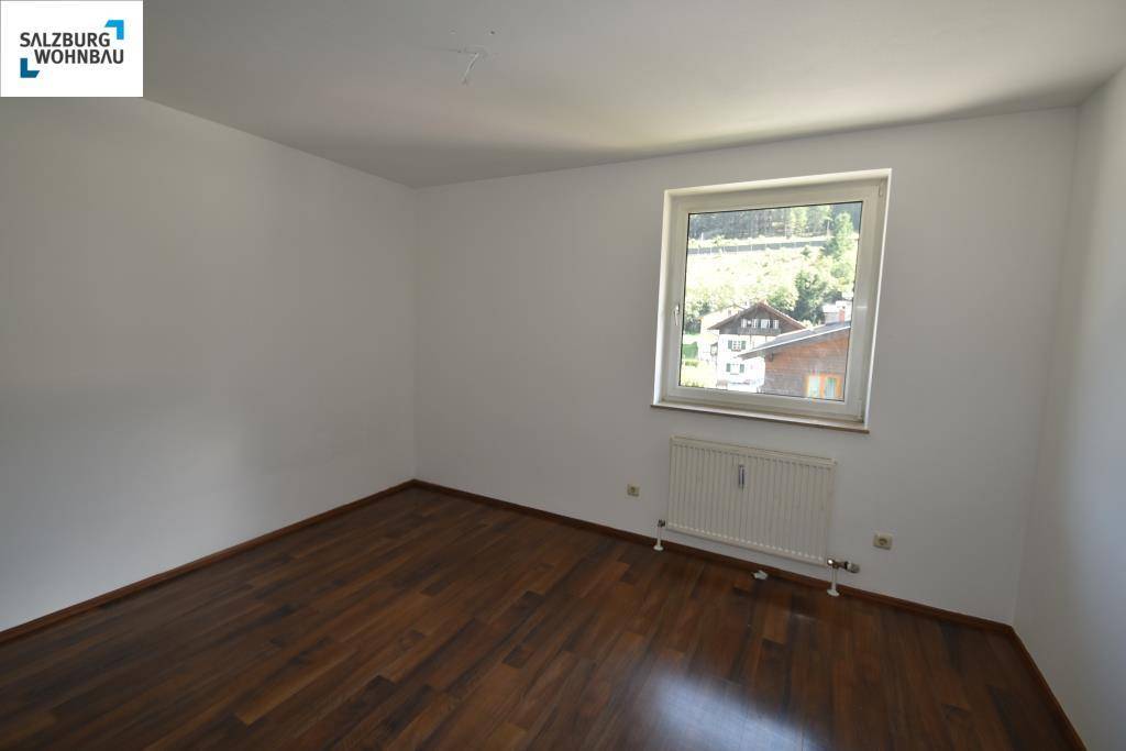 Helles Zimmer mit dunklem Laminatboden, weißen Wänden und einem Fenster mit Blick ins Grüne.