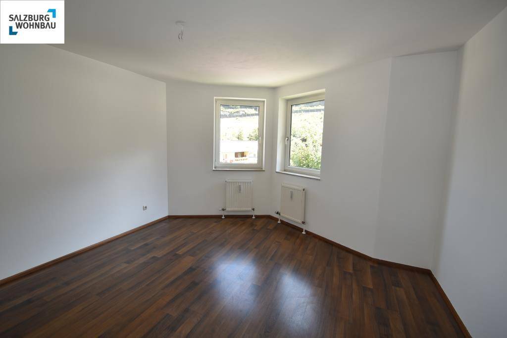 Leeres Schlafzimmer mit dunklem Laminatboden, weißen Wänden und zwei Fenstern.