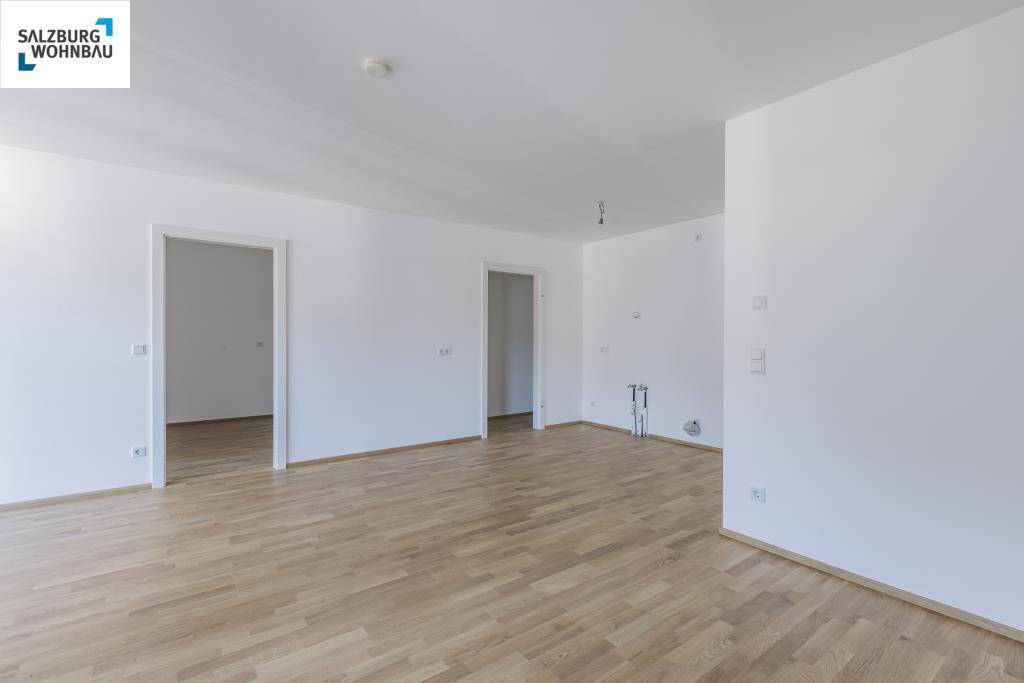 Geräumiger, unmöblierter Wohnbereich mit hellem Parkettboden und mehreren Türen.