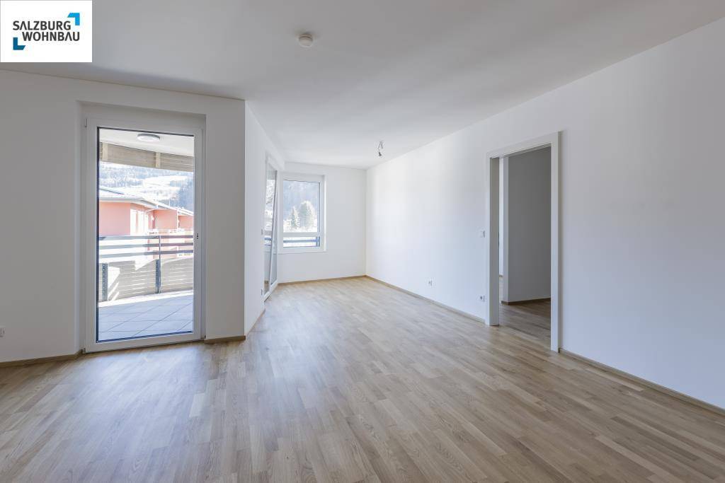 Geräumiges, unmöbliertes Wohnzimmer mit hellem Parkettboden und Zugang zum Balkon.