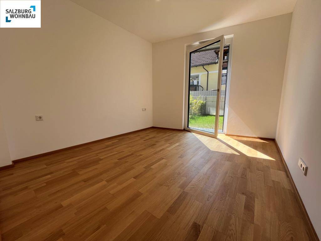 Helles Schlafzimmer mit Parkettboden und Fenster, das einen Blick ins Grüne bietet.