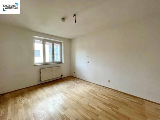 Helles Schlafzimmer mit Parkettboden und einem Fenster, das für angenehmes Tageslicht sorgt und weiße Wände hat.