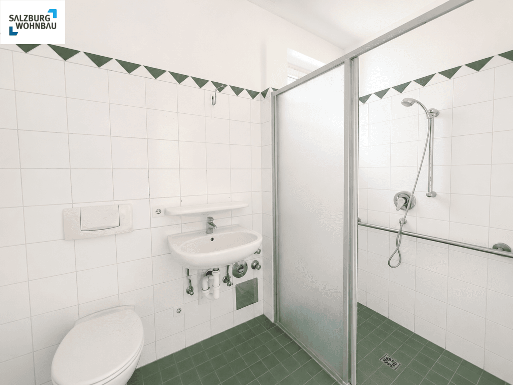 Barrierefreies Badezimmer mit Dusche, WC, Waschbecken und Haltegriffen, ausgestattet mit weißen und grünen Fliesen.