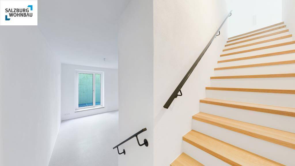 Heller Flur mit moderner Holztreppe und schwarzem Geländer, führt zu weiteren Räumen.