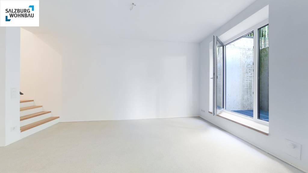 Geräumiger, heller Raum mit großen Fenstern und Zugang zum Außenbereich, teilweise mit Treppe.