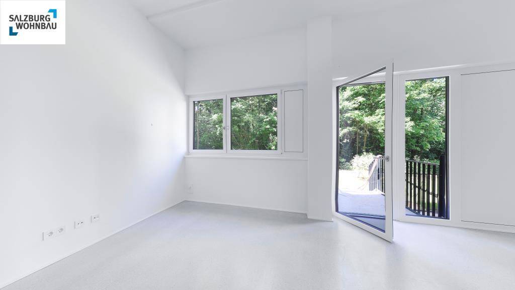 Heller Wohnraum mit großen Fenstern, weiß gestrichenen Wänden und Zugang zu einem Balkon mit Grünblick.