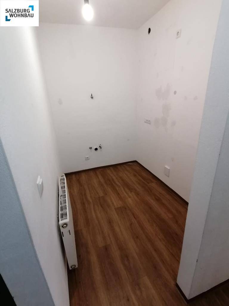 Kleiner, leerer Raum mit Laminatboden, Heizkörper und Anschlüssen, ideal als Abstellraum.
