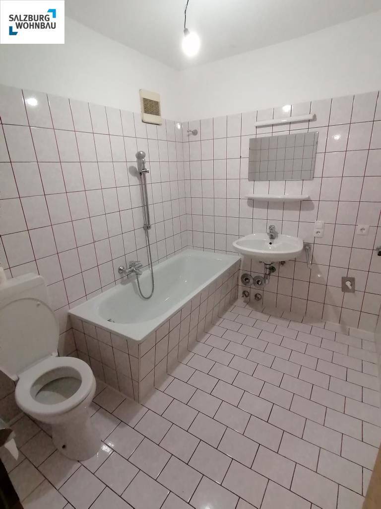Badezimmer mit weißen Fliesen, Badewanne mit Duschfunktion und einem einzelnen Waschbecken.
