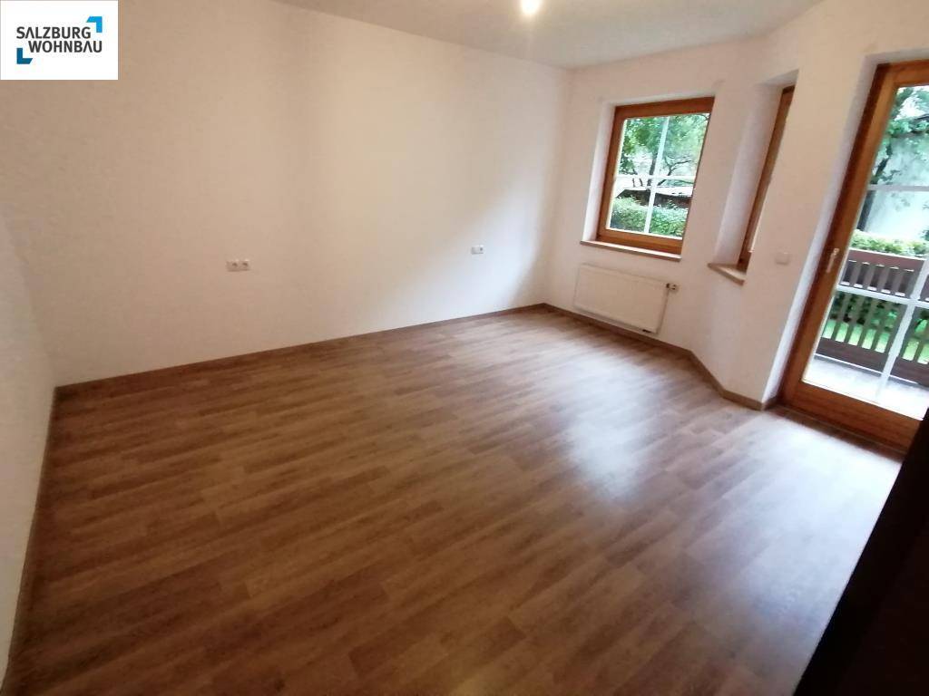 Leeres Schlafzimmer mit Laminatboden, hellen Wänden und direktem Zugang zu einem Balkon.