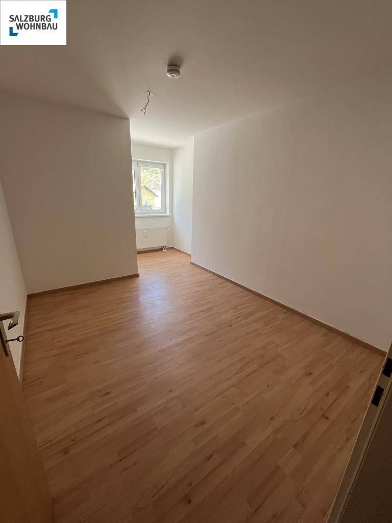 Helles Schlafzimmer mit Parkettboden und Fenster, bereit zur individuellen Gestaltung.