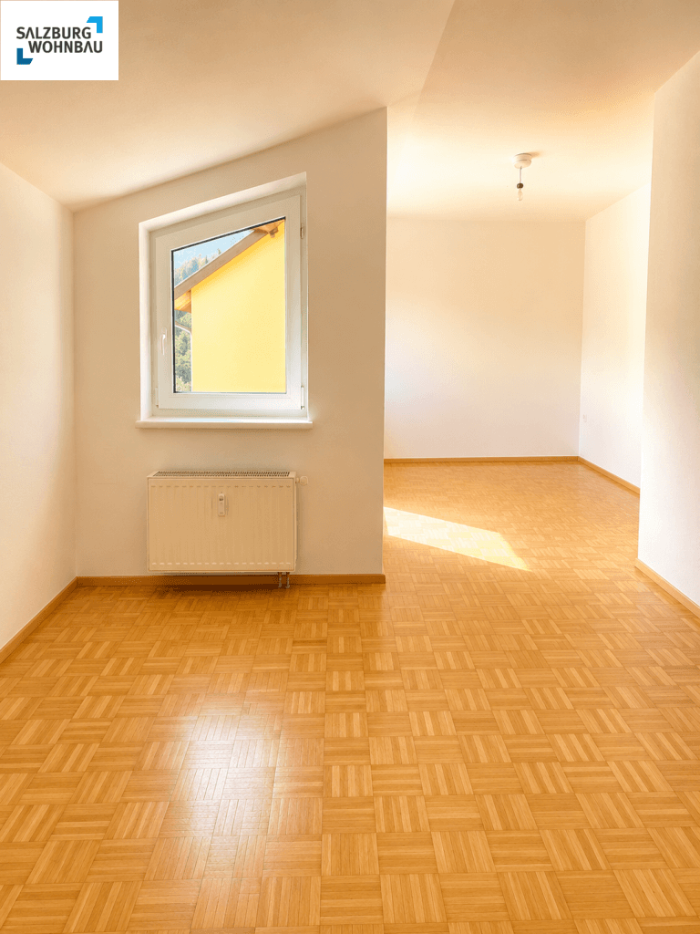 Lichtdurchfluteter Wohnbereich mit Parkettboden und Fenster mit Blick ins Grüne.