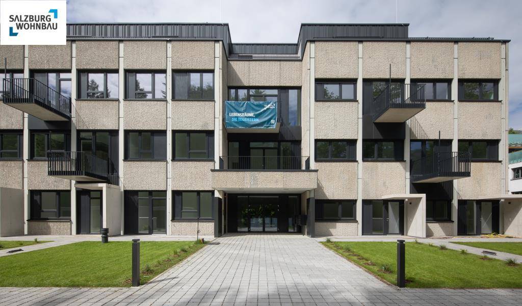 Moderne Wohnanlage mit schlichter Fassade, großen Fenstern und gepflegter Außenanlage.