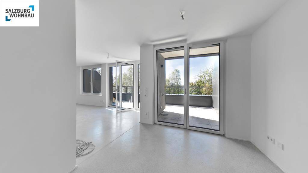 Lichtdurchfluteter Wohnbereich mit großen Schiebetüren zum Balkon und hellem Betonboden.