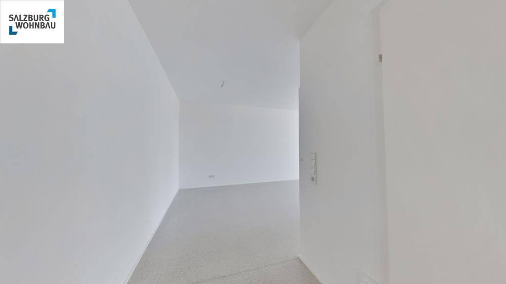 Leerer, heller Innenraum mit schlichten weißen Wänden und einem hellgrauen Laminatboden.