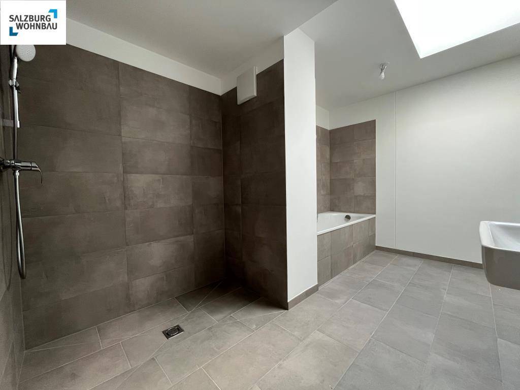 Modernes Badezimmer mit großer begehbarer Dusche, Badewanne und grauen Fliesen an Wänden und Boden.