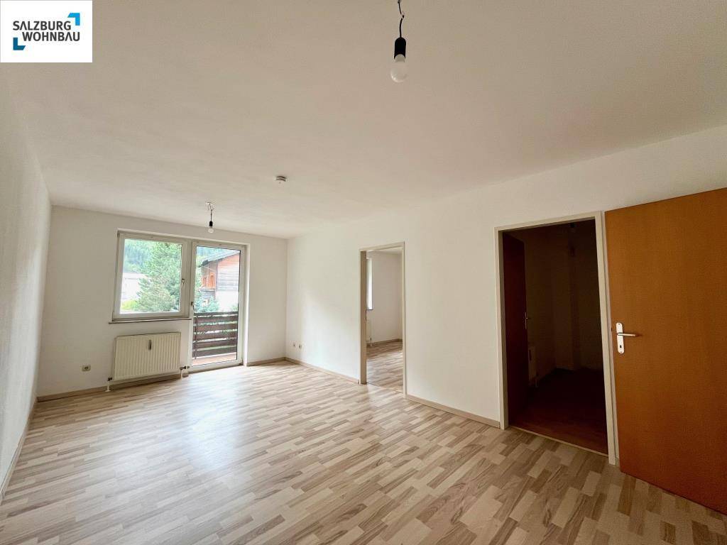 Helles Wohnzimmer mit Laminatboden und Zugang zu einem Balkon.