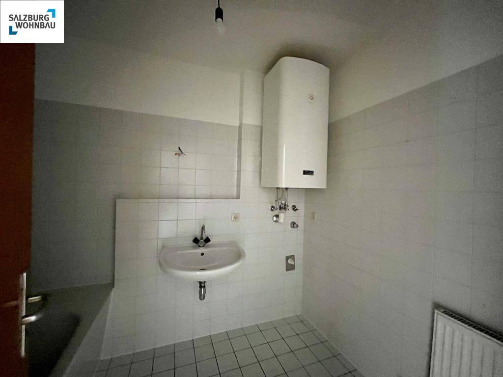 Badezimmer mit Badewanne, Waschbecken und Wandfliesen in hellem Grau.