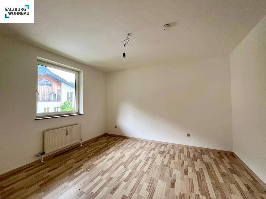 Helles Zimmer mit Laminatboden, Heizkörper und Blick nach draußen.