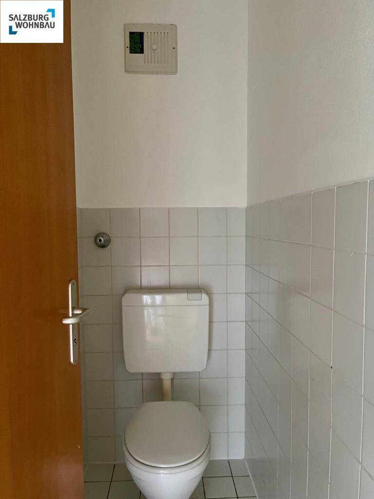 Separates WC mit Toilette und hellen Wand- und Bodenfliesen.