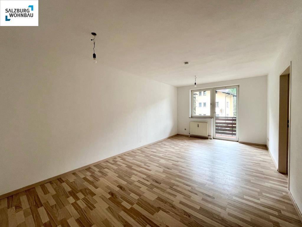 Geräumiges Wohnzimmer mit Laminatboden und Fenster mit Blick ins Grüne.