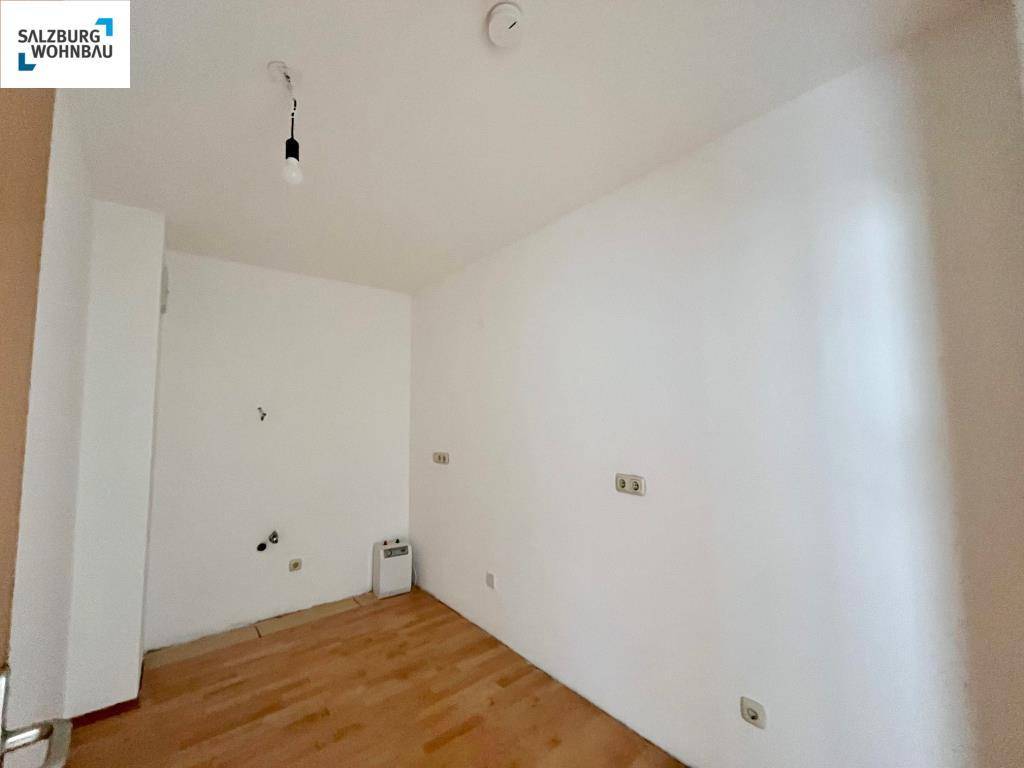 Leerer Küchenraum mit Anschlüssen für Geräte und Laminatboden.