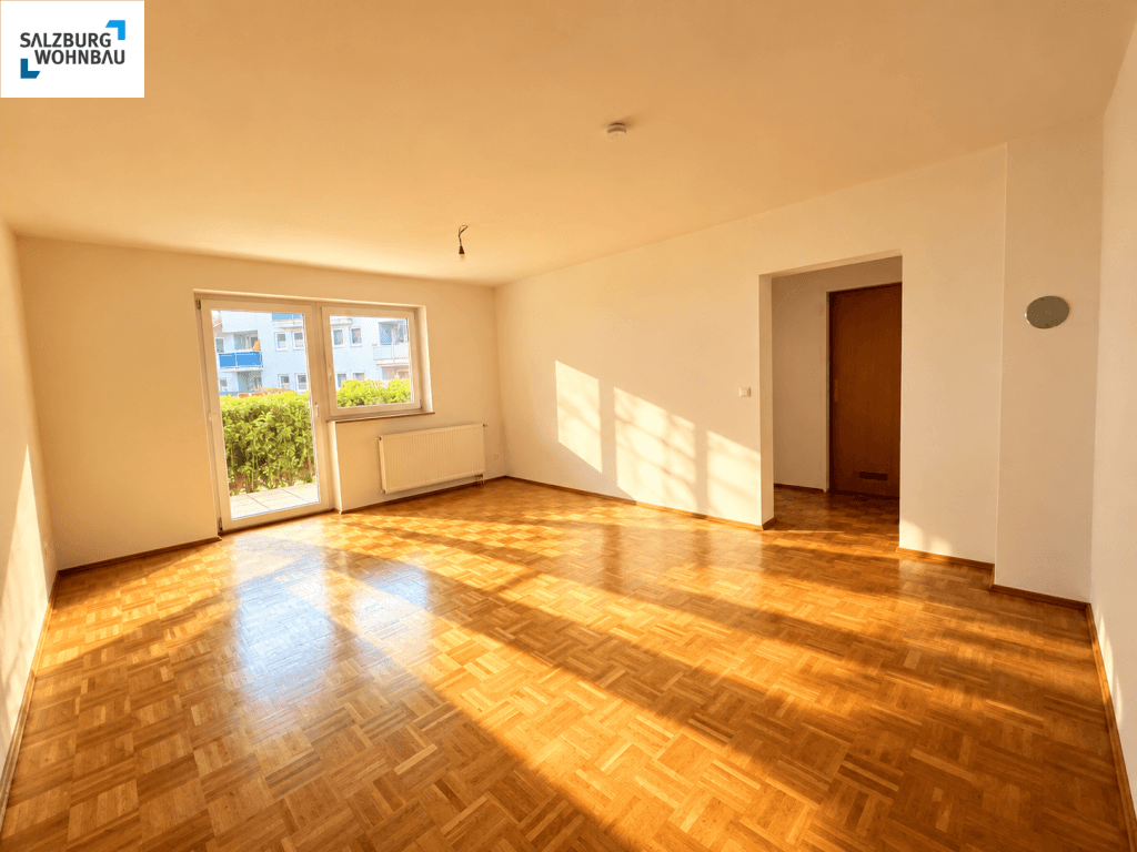Helles, leeres Wohnzimmer mit Fischgrätparkettboden und Zugang zu einem sonnigen Balkon.