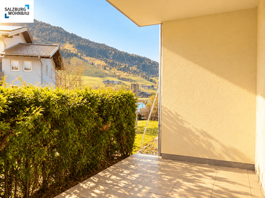 Sonnige Terrasse mit Hecke und weitem Blick auf die umliegende Berglandschaft.