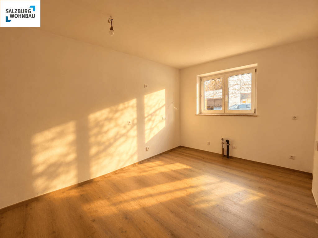 Leerer Küchenraum mit Holzfußboden und sichtbaren Anschlüssen für eine zukünftige Einbauküche.