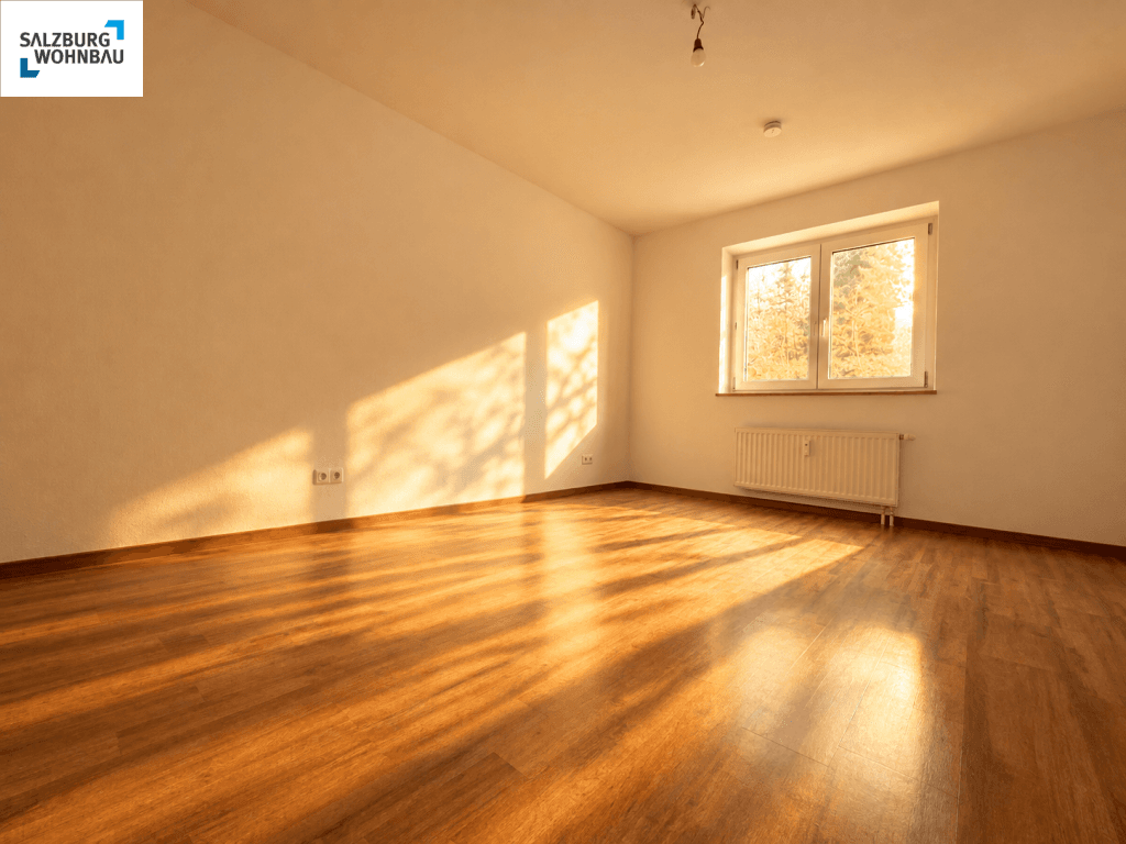 Sonniges, unmöbliertes Schlafzimmer mit Holzfußboden und einem großen Fenster.